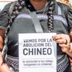 una mujer indígena sostiene un panfleto que dice "vamos por la abolición del chineo. la violación a las niñas indígenas es criminal"